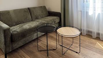 A modern living room with a green sofa, two small round tables, and a large window with sheer curtains.