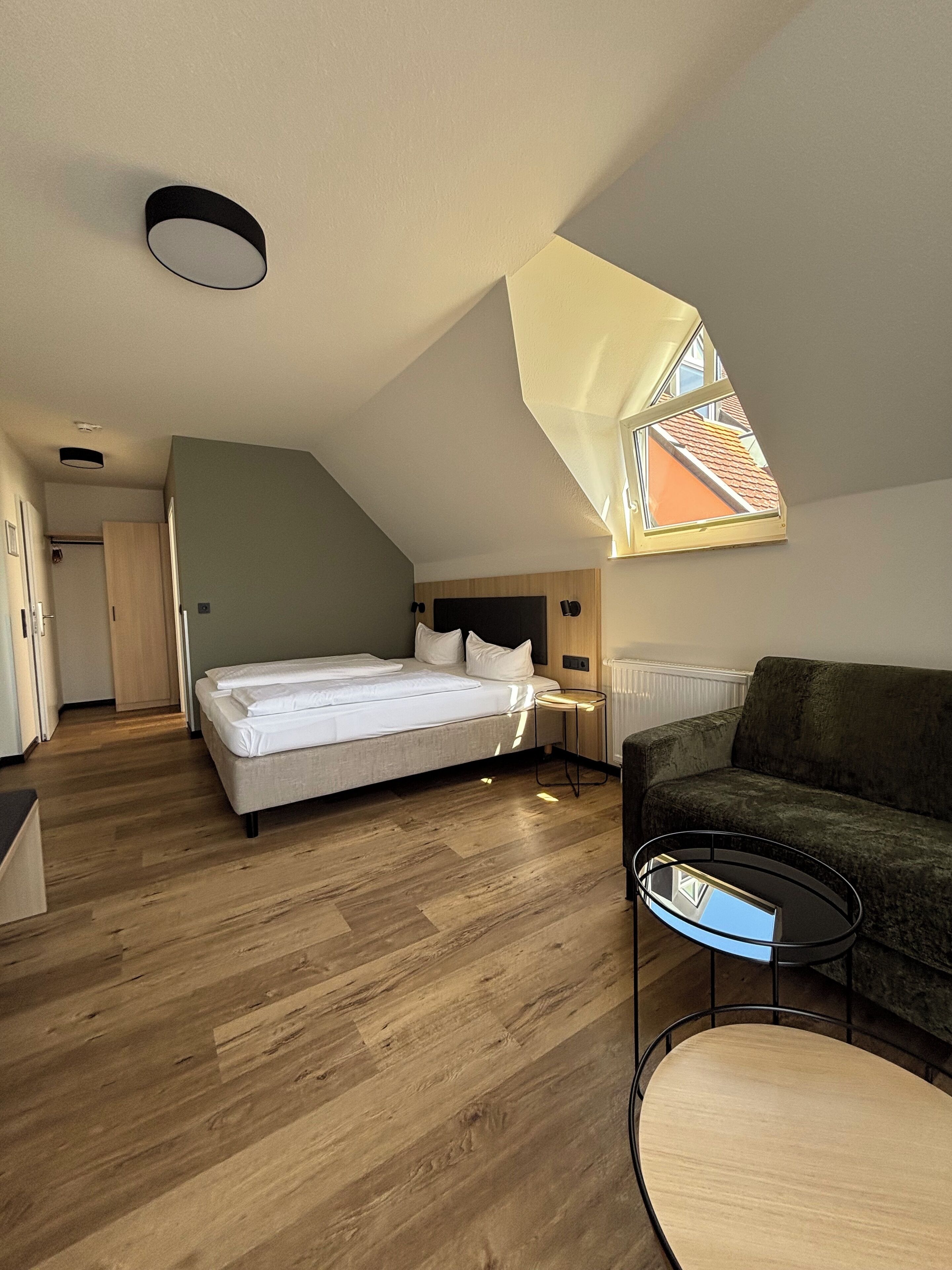 A modern, well-lit room with a bed, a sofa, a small table, and a skylight.