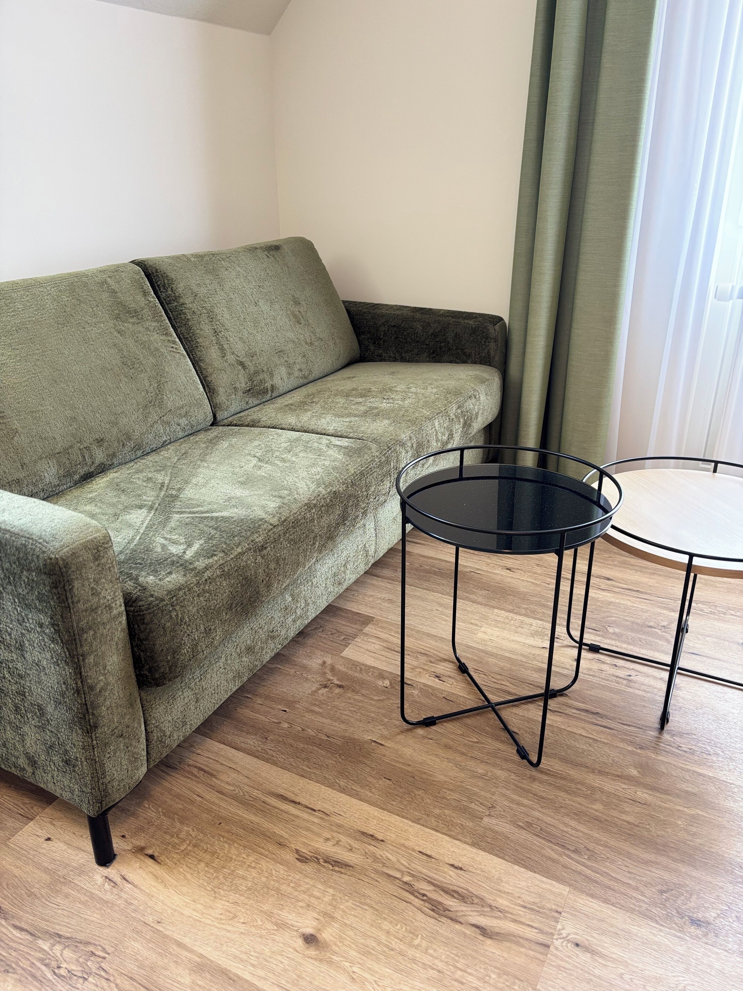 Un sofá verde y una mesita redonda con estructura negra en una habitación con suelo de madera.