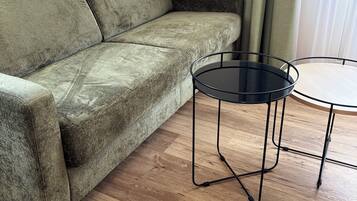 A green sofa and a small round table with a black frame in a room with wooden flooring.