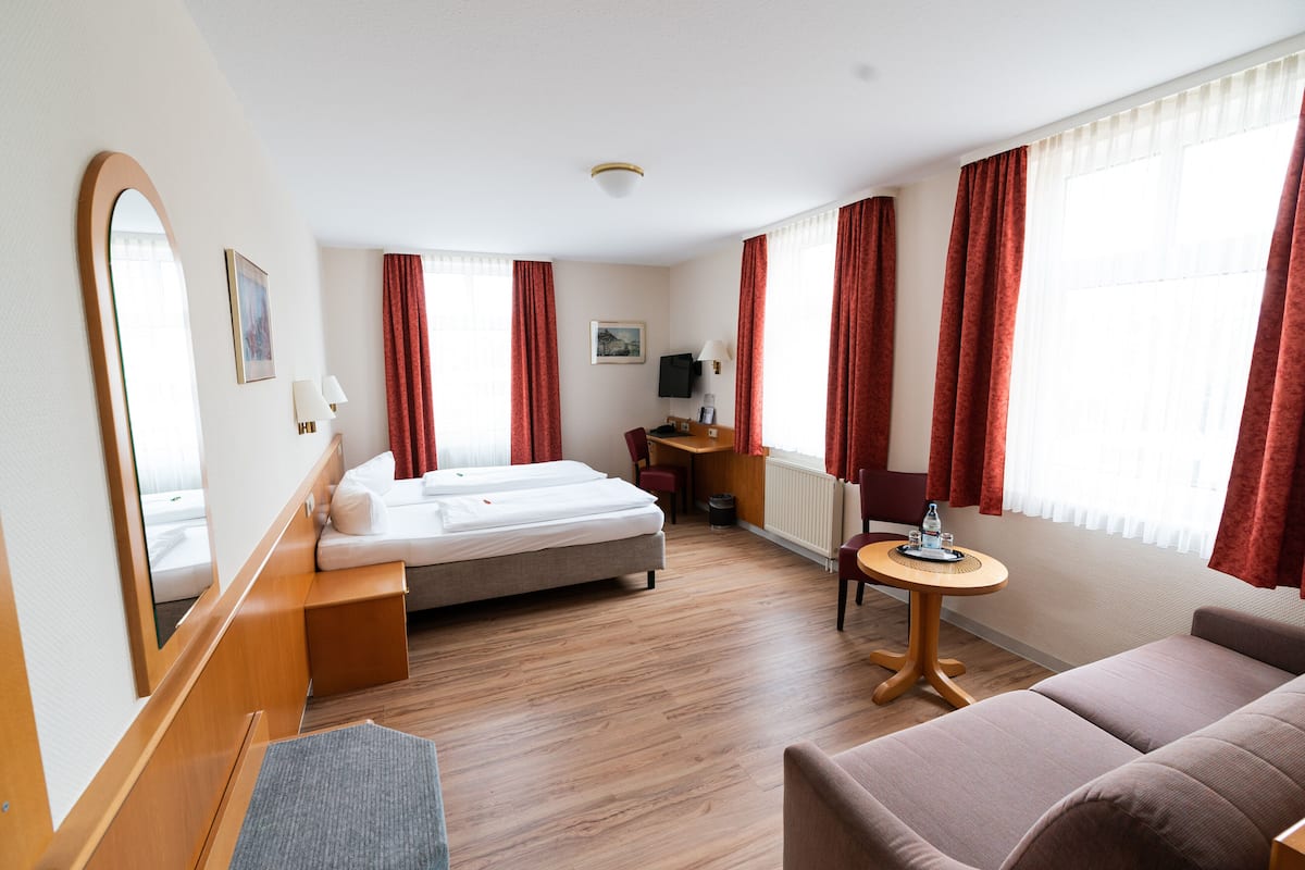 A hotel room with a bed, a sofa, a small table, and a desk.