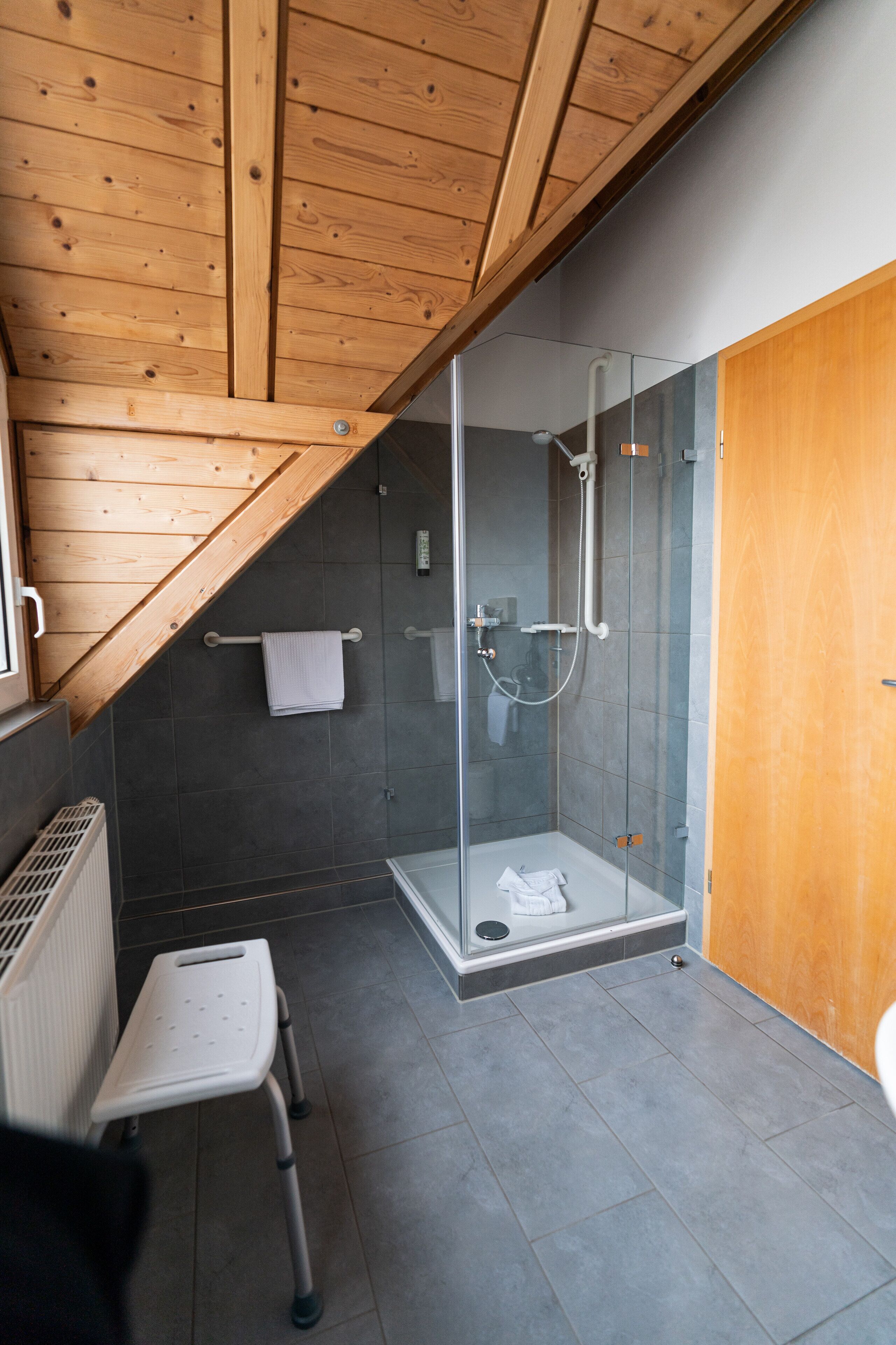 Un baño moderno con ducha de vidrio, techo de madera y un taburete.