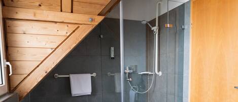 Un baño moderno con ducha de vidrio, techo de madera y un taburete.