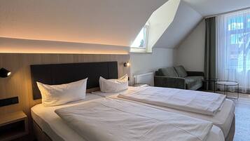 A hotel room with two beds, a sofa, a small table, and a window with curtains.