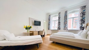 A hotel room with two beds, a desk, a TV, and a window with curtains.