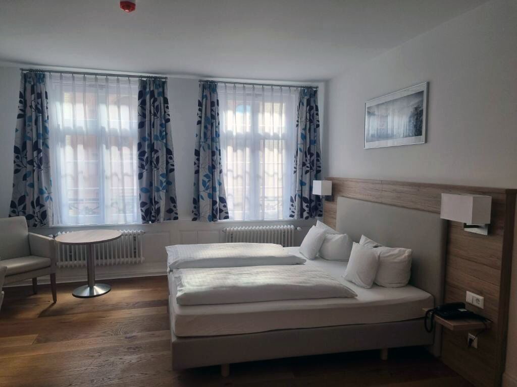 A hotel room with a bed, a chair, a small table, and a radiator.