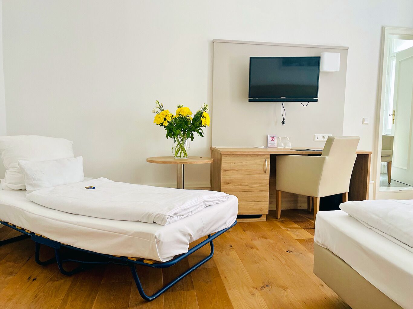Ein Hotelzimmer mit einem Bett, einem Schreibtisch, einem Sessel, einem Fernseher und einer Vase mit Blumen.