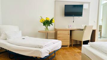 Ein Hotelzimmer mit einem Bett, einem Schreibtisch, einem Sessel, einem Fernseher und einer Vase mit Blumen.