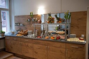 Una barra de buffet con diversas opciones de comida y bebidas, entre ellas frutas, verduras y pan.