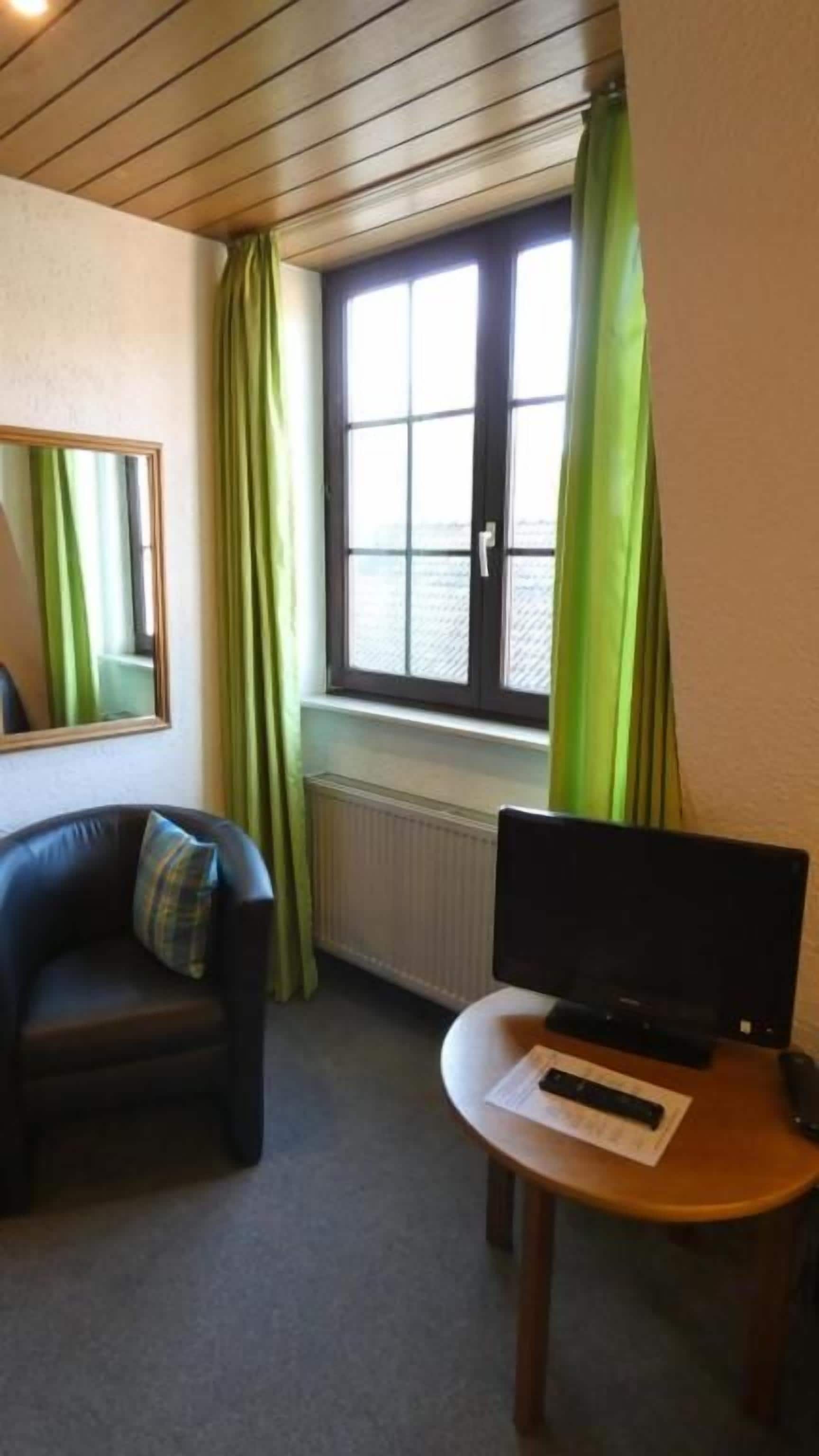 Una habitación con un sofá, una mesita con una computadora portátil, una ventana con cortinas y un radiador.