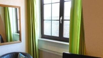 Una habitación con un sofá, una mesita con una computadora portátil, una ventana con cortinas y un radiador.