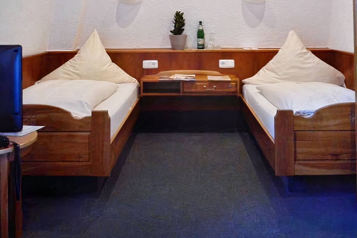 Une petite pièce accueillante, avec deux lits en bois, une petite table ornée d’une plante et d’une bouteille, et une chaise.