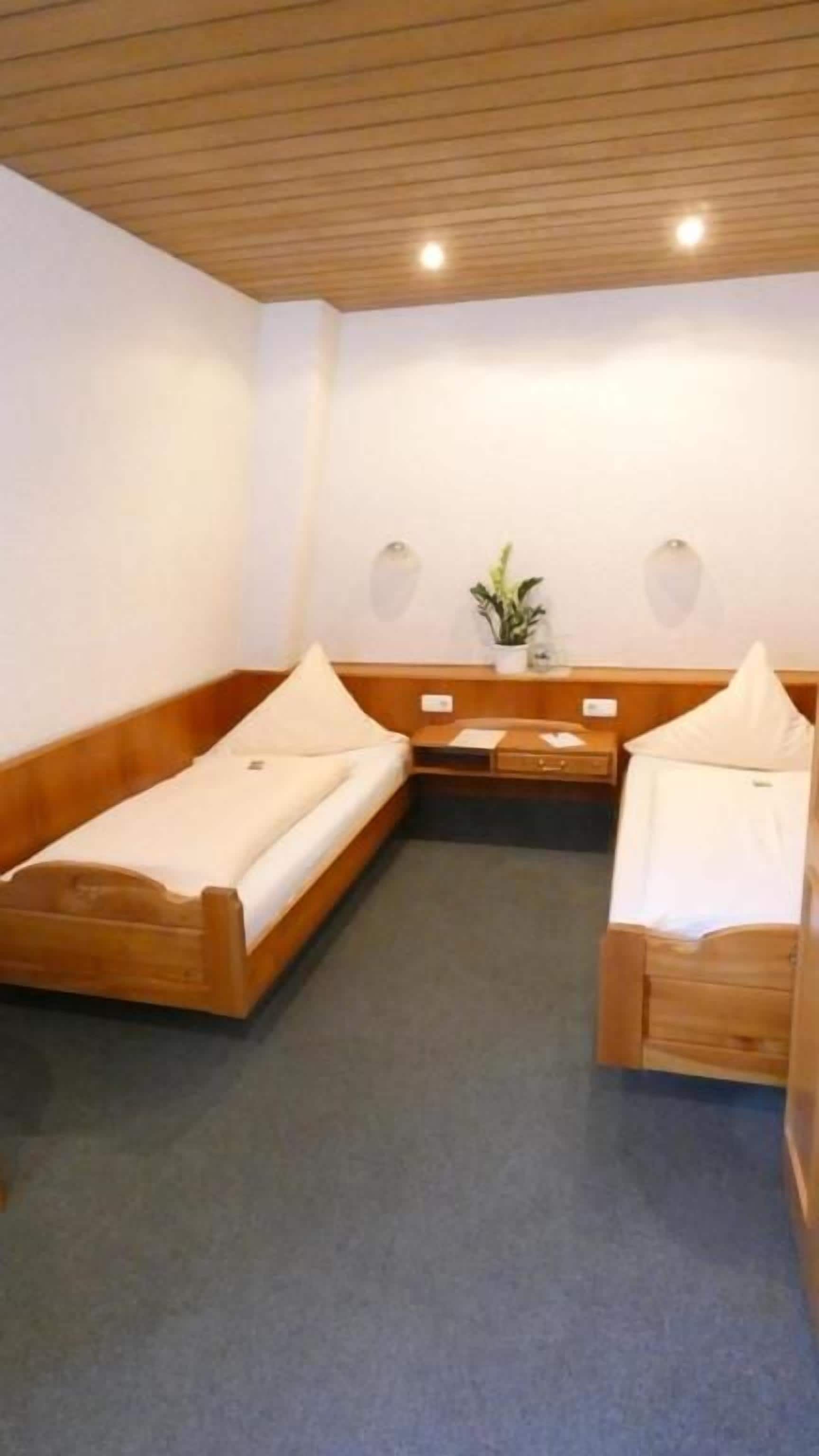Ein Zimmer mit zwei Holzbetten, einem kleinen Tisch mit Pflanze und einer Wandleuchte.