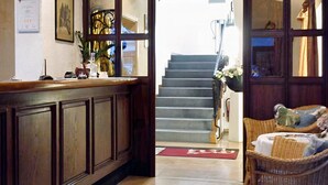 A wooden interior with a staircase leading to an upper floor, a reception desk, and wicker furniture.
