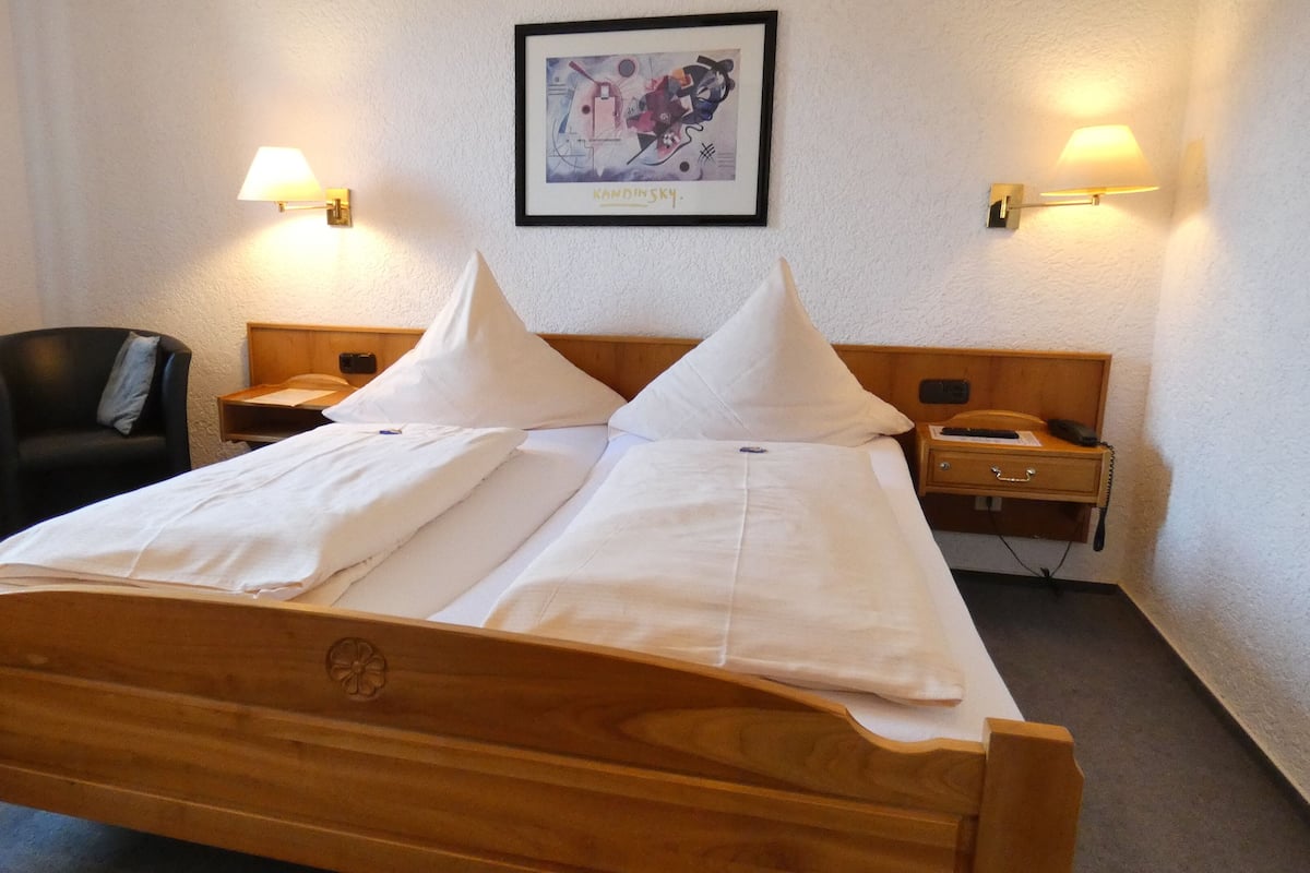 Une chambre d’hôtel avec un lit en bois, deux tables de chevet, une chaise et une œuvre d’art encadrée au mur.
