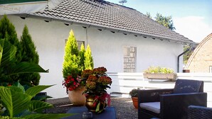 A patio with outdoor furniture, potted plants, and a building with a tiled roof.