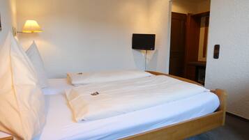 Cama de casal com roupa de cama branca num quarto com parede texturizada, luminária presa à parede e porta fechada.