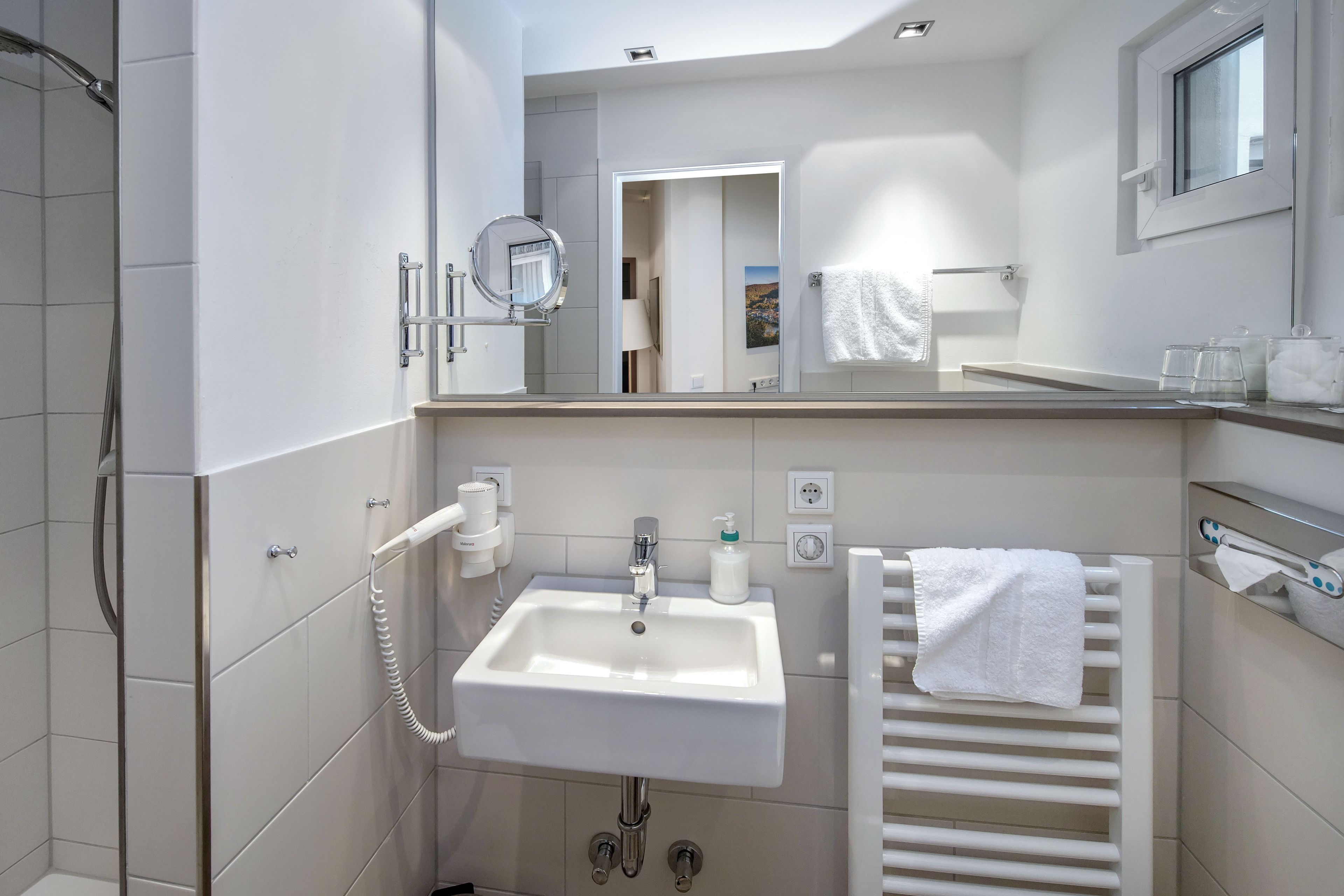 A modern bathroom with a white sink, a mirror, a towel rack, and a shower.