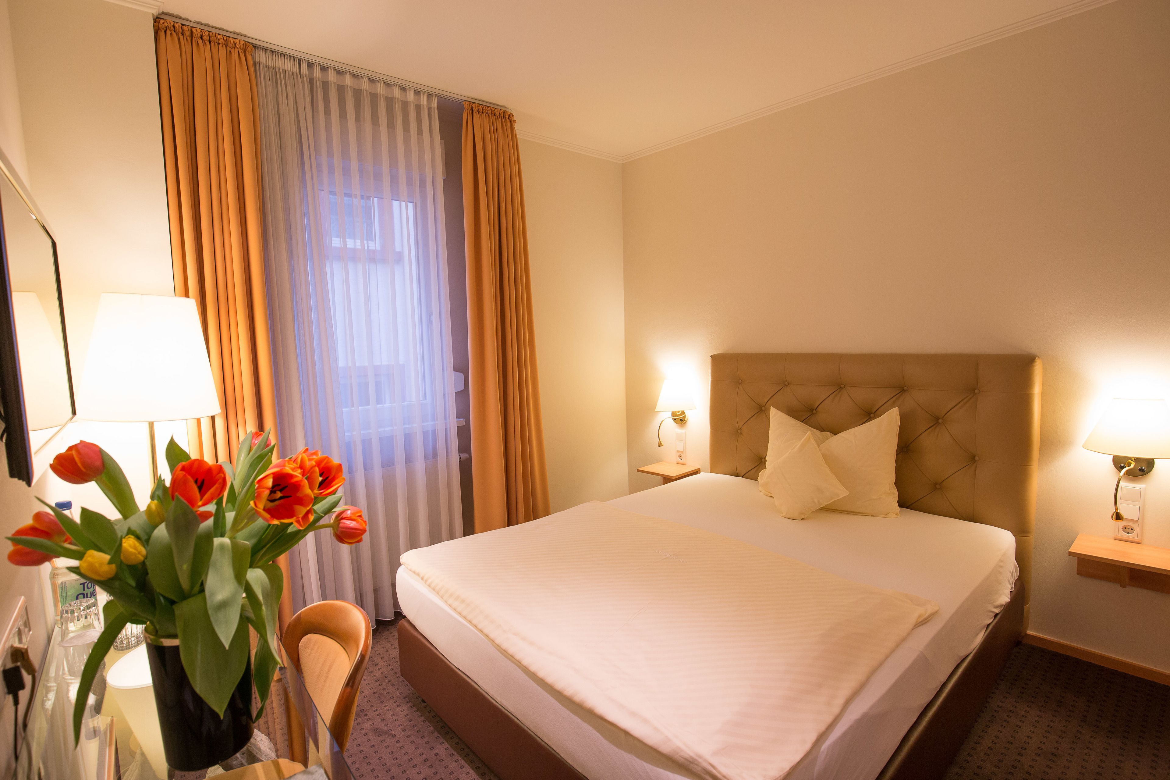 Ein Hotelzimmer mit einem großen Bett, zwei Nachttischlampen, einem Nachttisch, einem Sessel und einer Vase mit Tulpen.