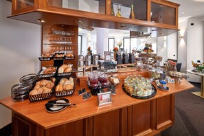 Un buffet proposant une variété d’aliments et de boissons, notamment du pain, des pâtisseries et des fruits.