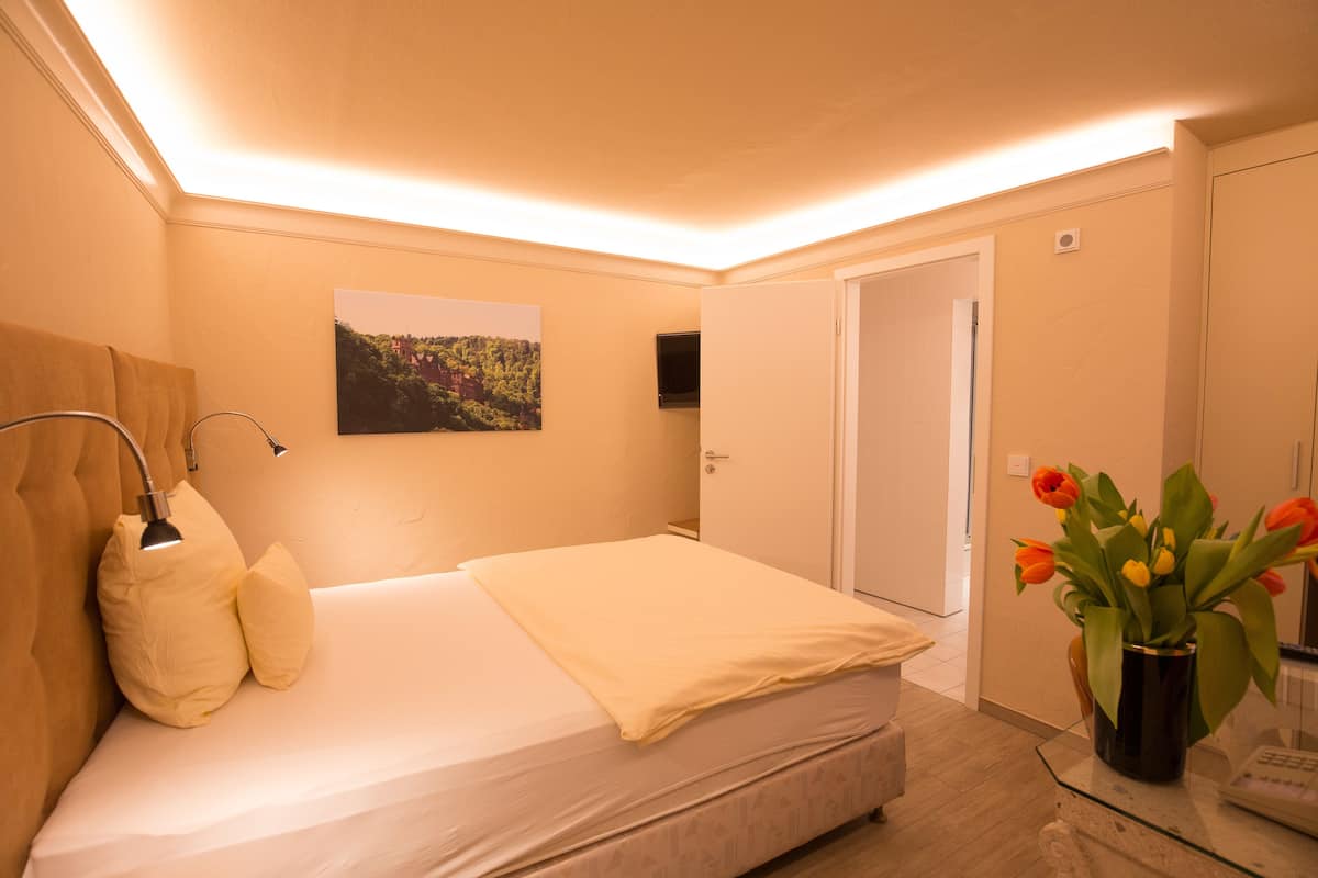 A hotel room with a bed, a bedside lamp, a picture on the wall, and a vase with flowers.