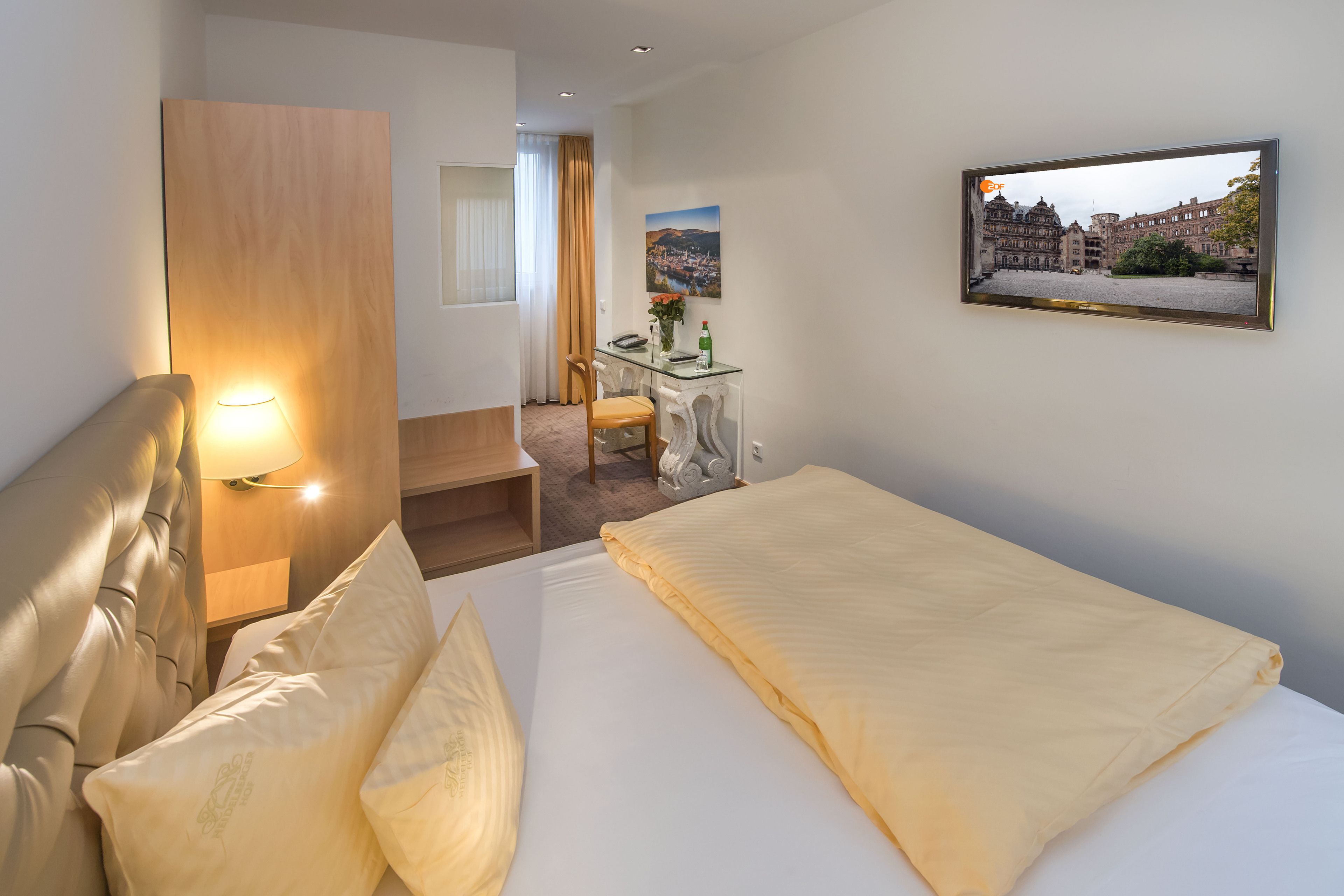 A hotel room with a bed, a desk, a chair, a TV, and a window with curtains.