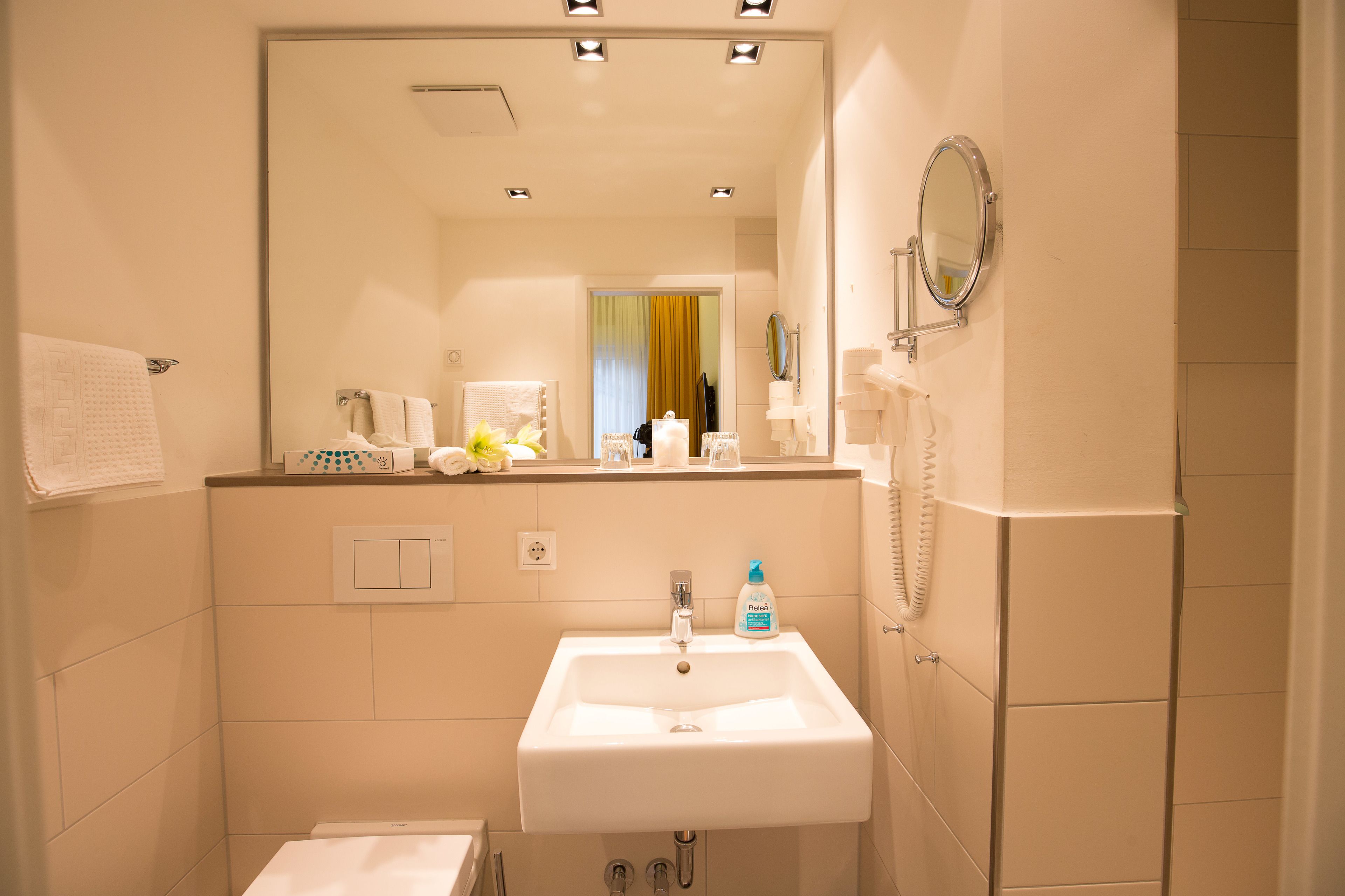 A bathroom with a white sink, mirror, and towel rack. There is a bottle of hand soap on the sink.