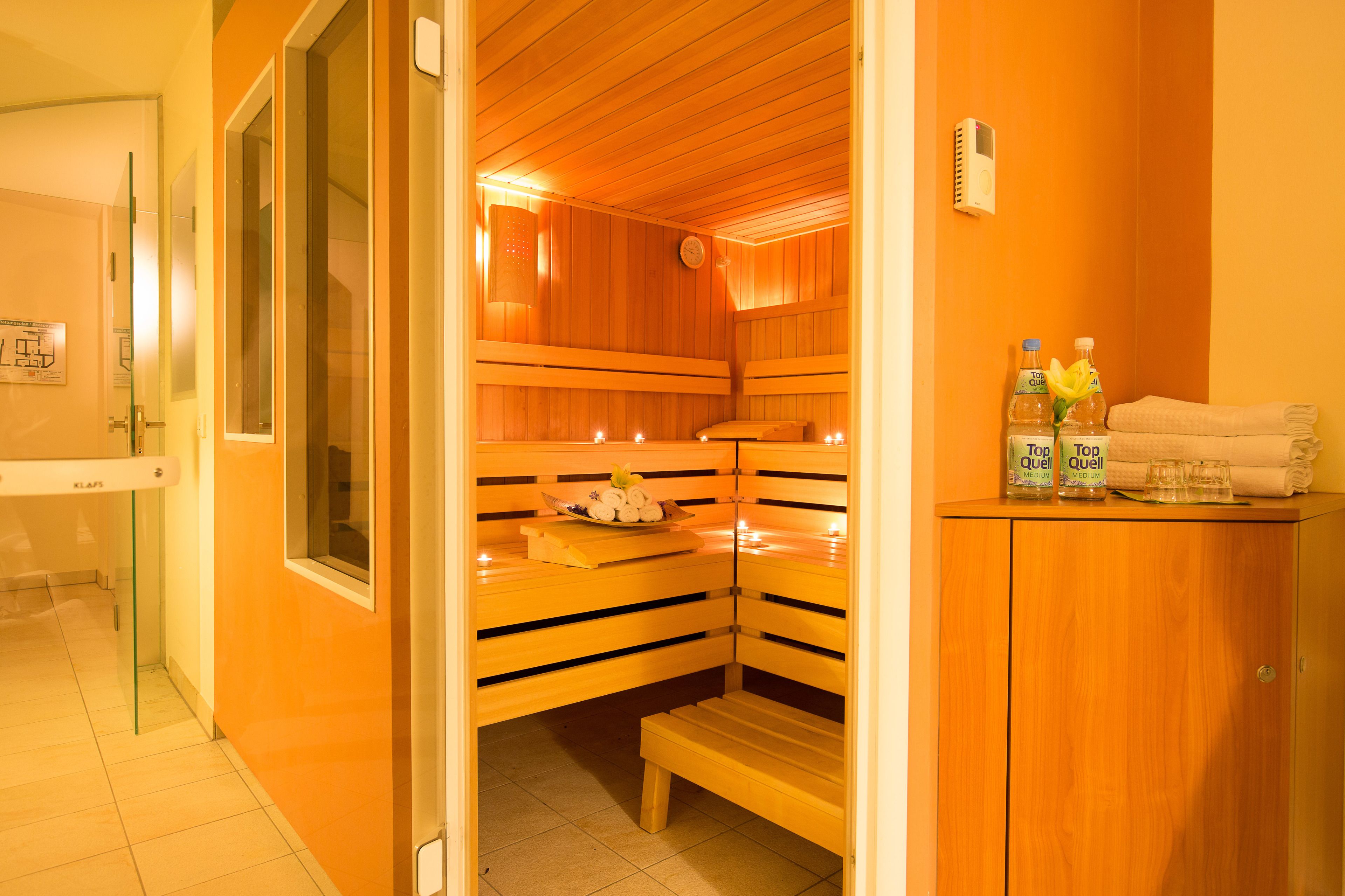 A sauna room with wooden benches, a bench with a towel, and two bottles of Top Qual water on a table.