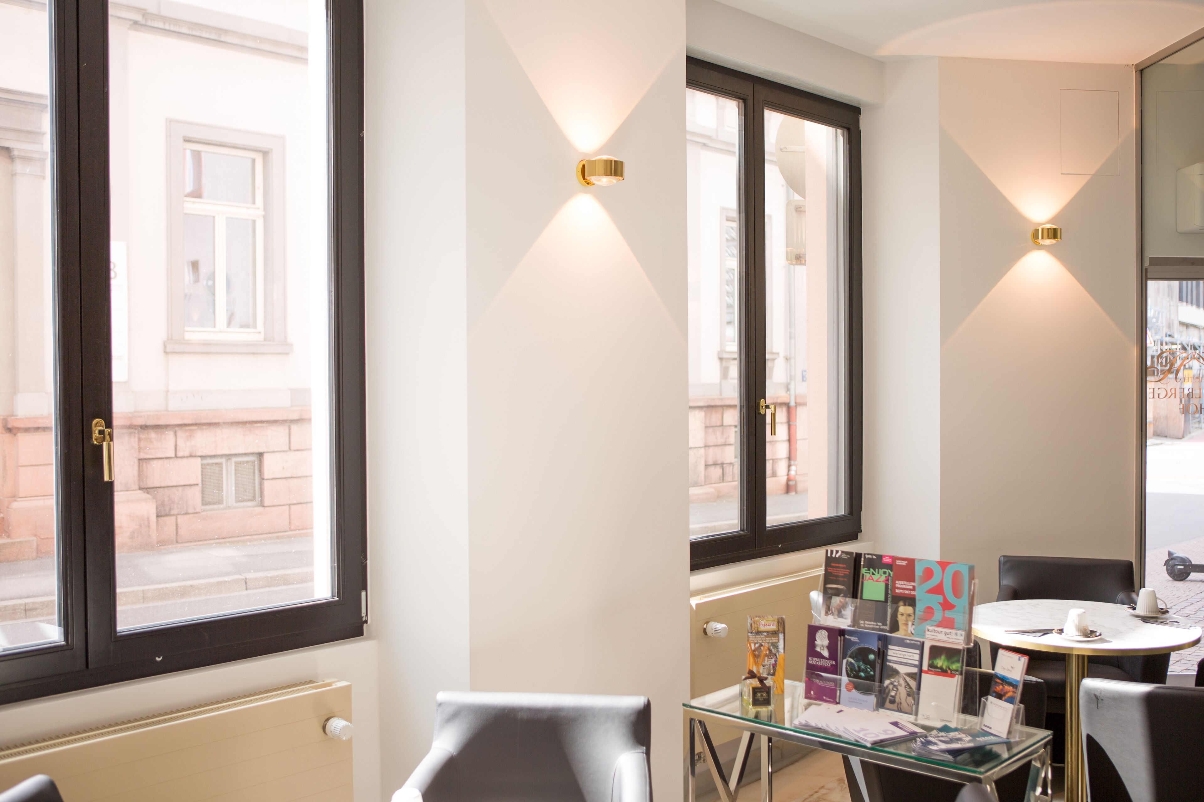 Habitación de hotel con un ventanal grande, una mesa de vidrio con revistas y una silla.
