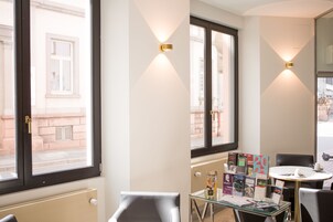 Habitación de hotel con un ventanal grande, una mesa de vidrio con revistas y una silla.