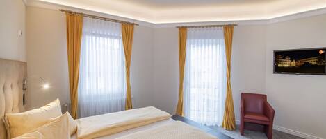 A hotel room with a large bed, two bedside tables, a TV mounted on the wall, and a red chair.