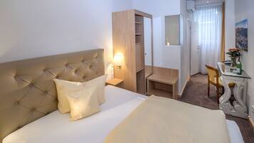 Ein Hotelzimmer mit einem großen Bett, einer Nachttischlampe, einem Holzschrank, einem Schreibtisch mit Stuhl und einem kleinen Tisch mit Blumen.
