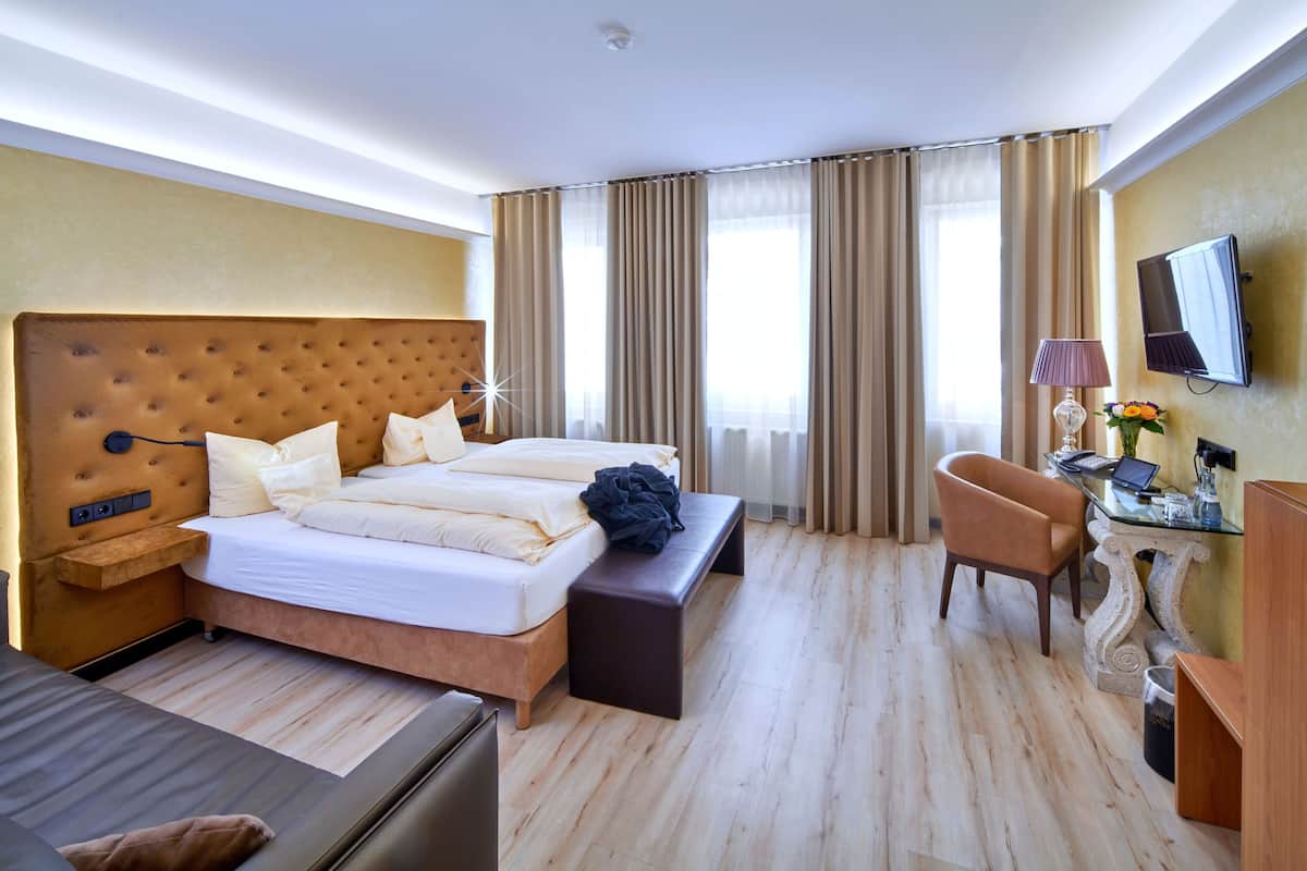 A hotel room with a large bed, a desk with a laptop, a chair, and a television on the wall.