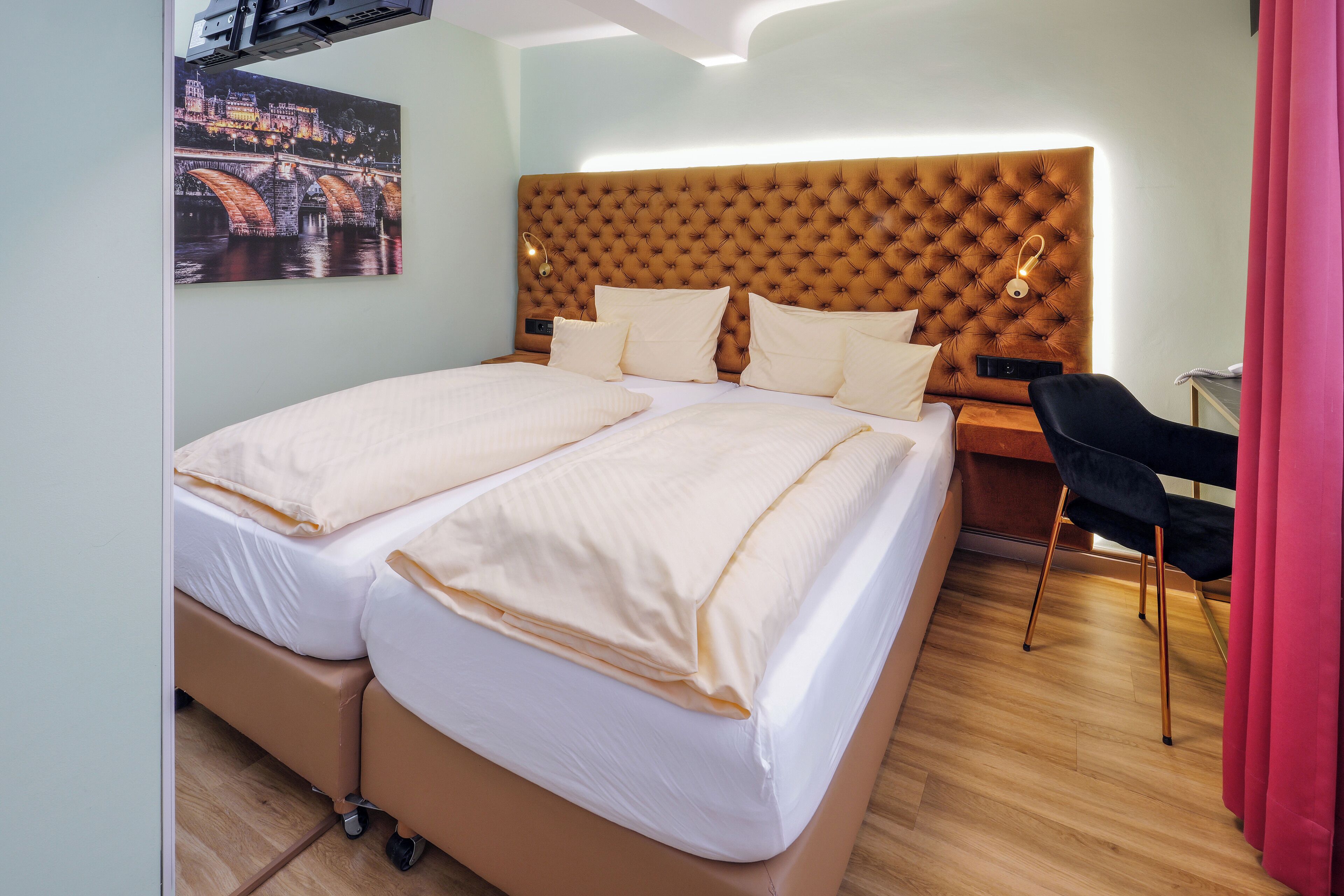 A double bed with a tufted headboard, a bedside table with a lamp, and a chair.
