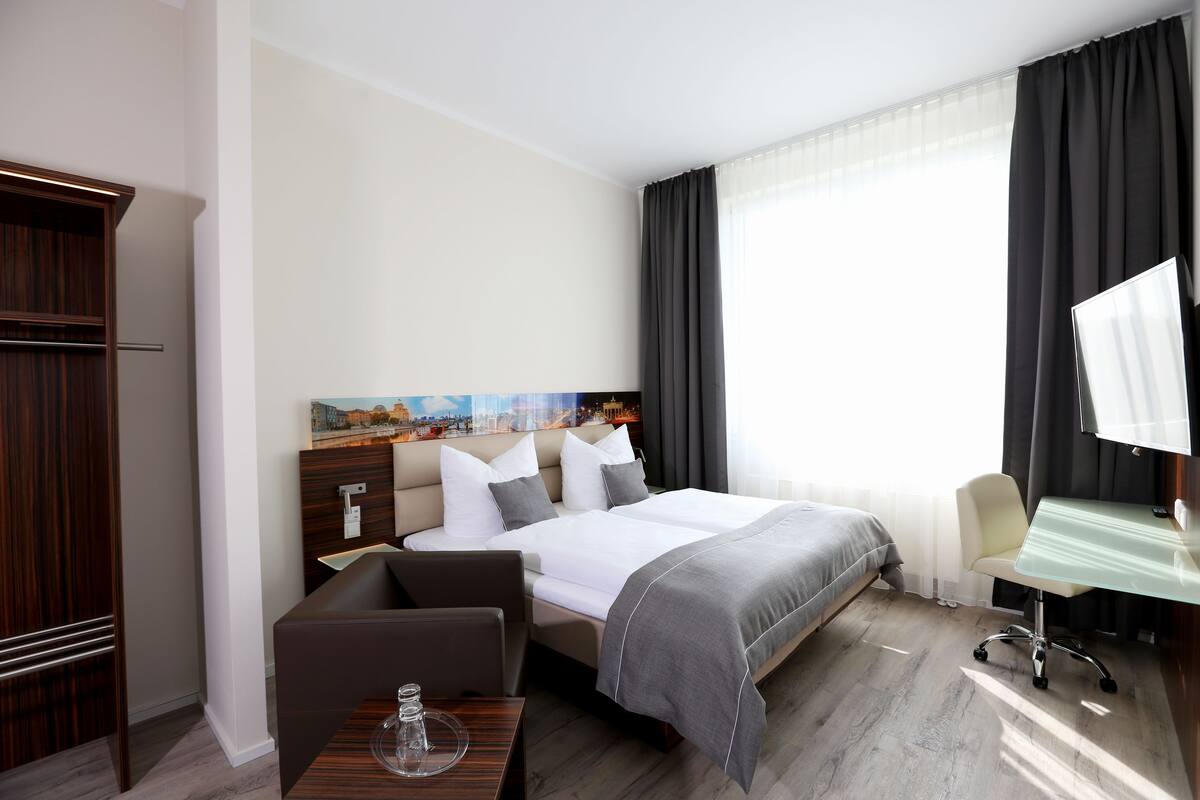 A hotel room with a bed, a desk, a chair, a small table, and a wardrobe.