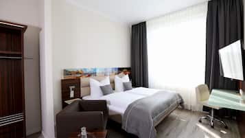 A hotel room with a bed, a desk, a chair, a small table, and a wardrobe.