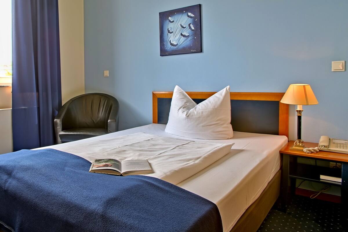 A neatly made bed with white bedding, a blue blanket, and a book on the bed.
