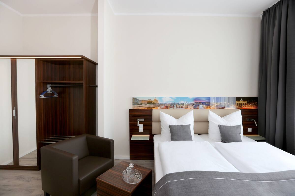 A hotel room with a bed, a sofa, a nightstand, a wardrobe, and a painting on the wall.