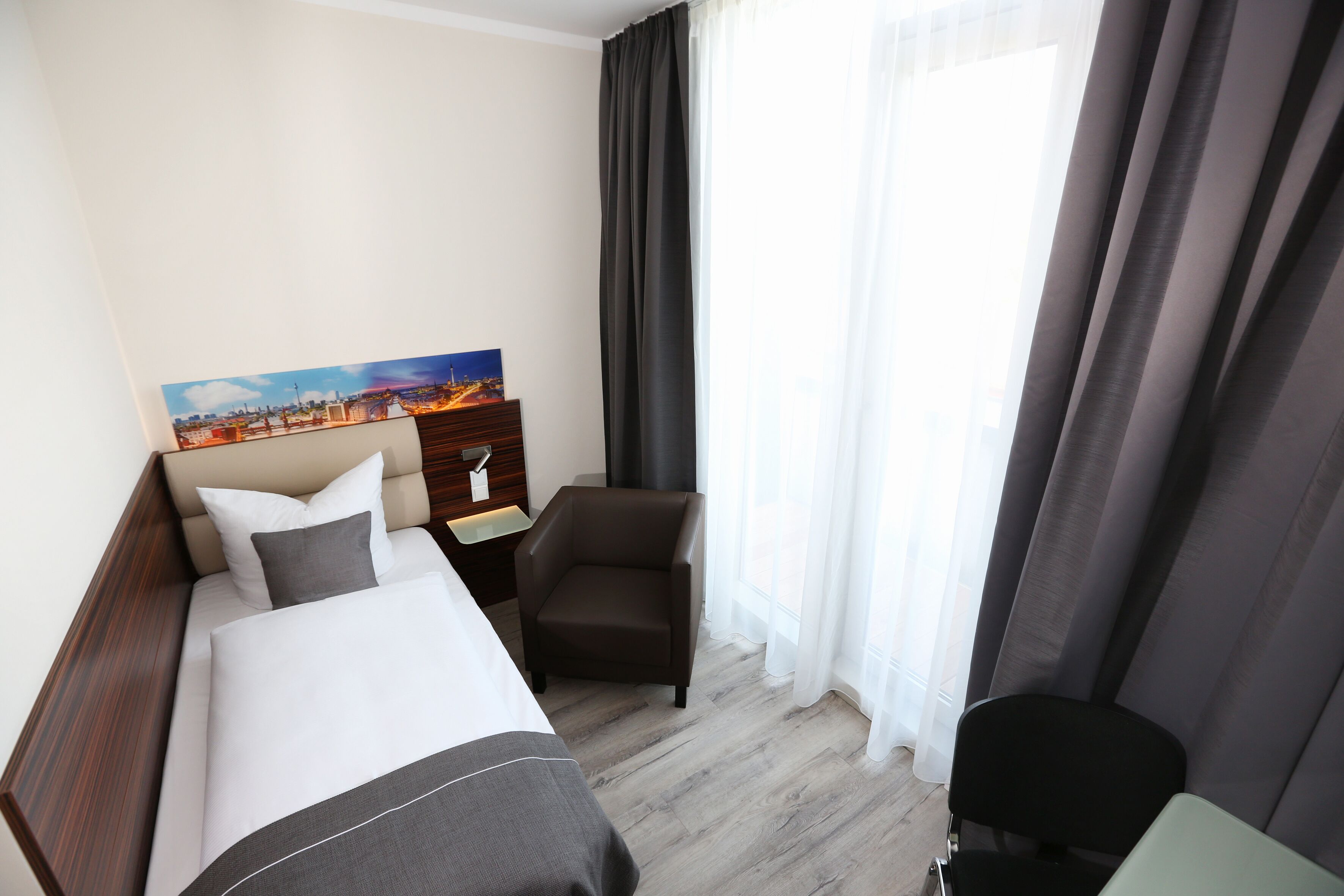 A hotel room with a bed, a chair, a nightstand, and a painting on the wall.