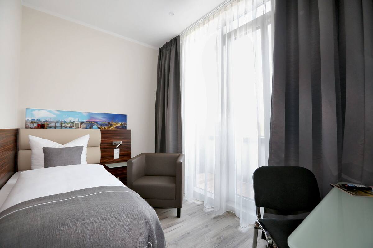 A hotel room with a bed, two chairs, a desk, and a painting on the wall.