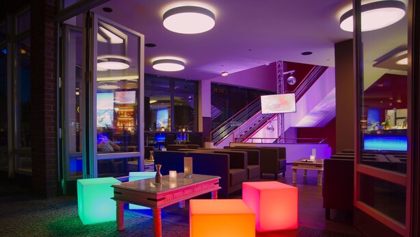A modern lounge area with seating, a bar, and a staircase. - Hoteltow (Teltow)