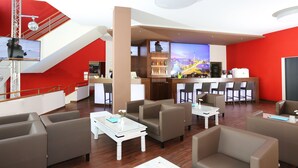 A modern hotel lobby with a red accent wall, a bar area, and comfortable seating. - Hoteltow (Teltow)