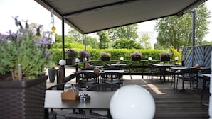 An outdoor patio area with tables and chairs, surrounded by greenery and potted plants. - Hotel Haus Fück (Leverkusen)
