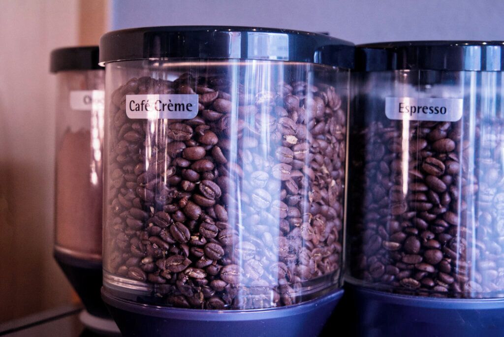 Tres recipientes etiquetados con granos de café, uno con la etiqueta 'Café Crème' y el otro 'Espresso'.