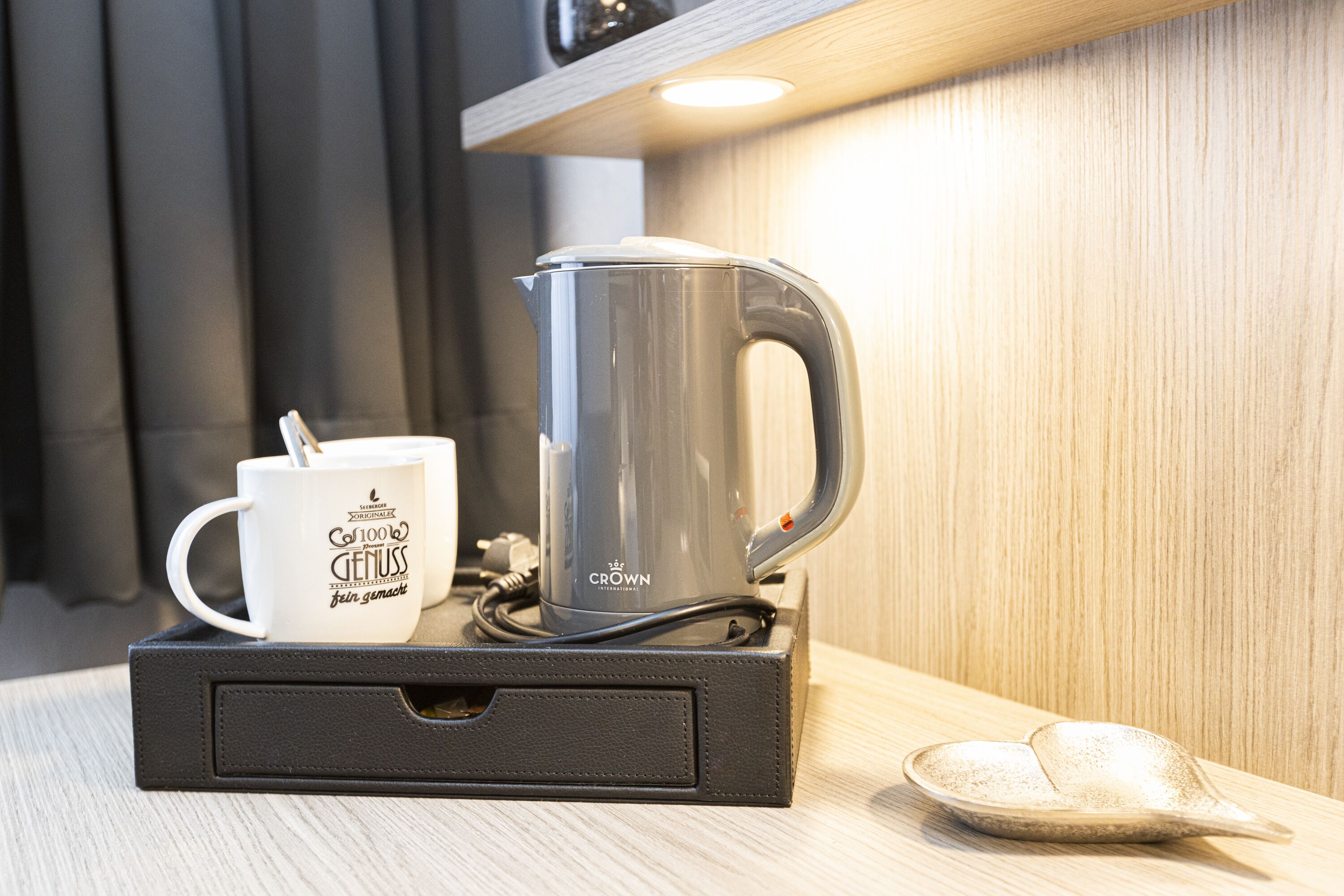 Eine Edelstahl-Kaffeemaschine und eine weiße Tasse mit Schriftzug auf einer schwarzen Ablagefläche.
