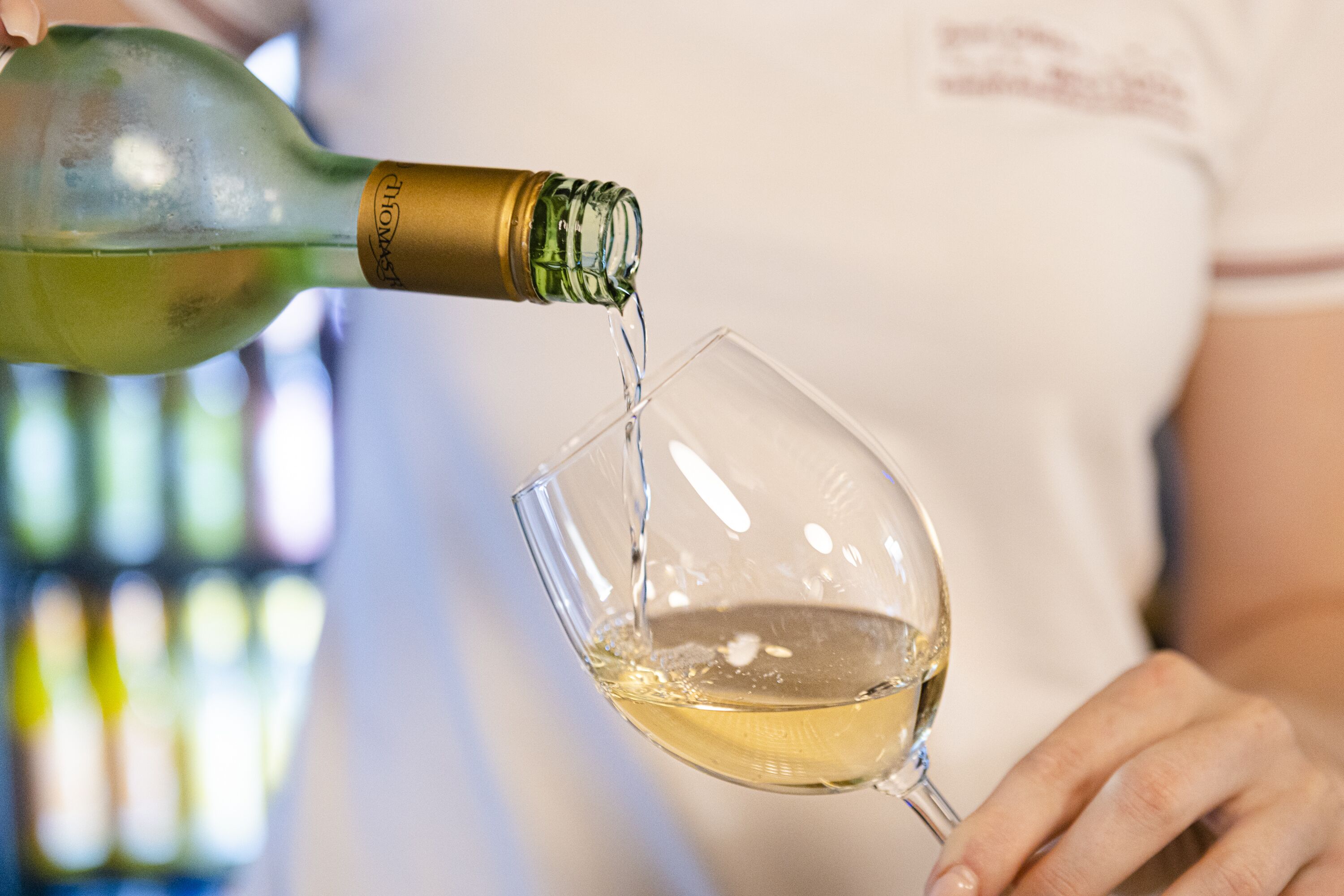 A person pouring white wine from a green bottle into a clear glass.