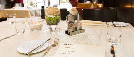 A dining table set with a menu, glasses, cutlery, and a decorative vase with a flower.