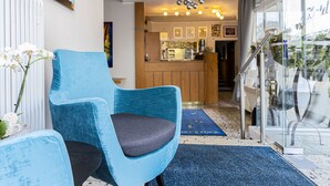 A hotel lobby with a blue armchair, a reception desk, and a view of the kitchen area. - Hotel Haus Fück (Leverkusen)