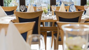 A restaurant setting with wooden chairs and tables, each set with a wine glass, a water glass, and a napkin. - Hotel Haus Fück (Leverkusen)