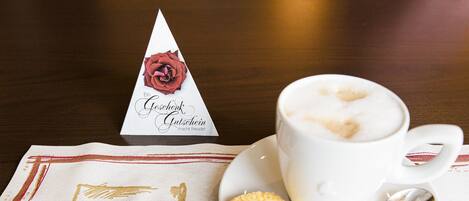 A cup of coffee with a heart-shaped foam on top, a biscuit, and a napkin with a heart design.